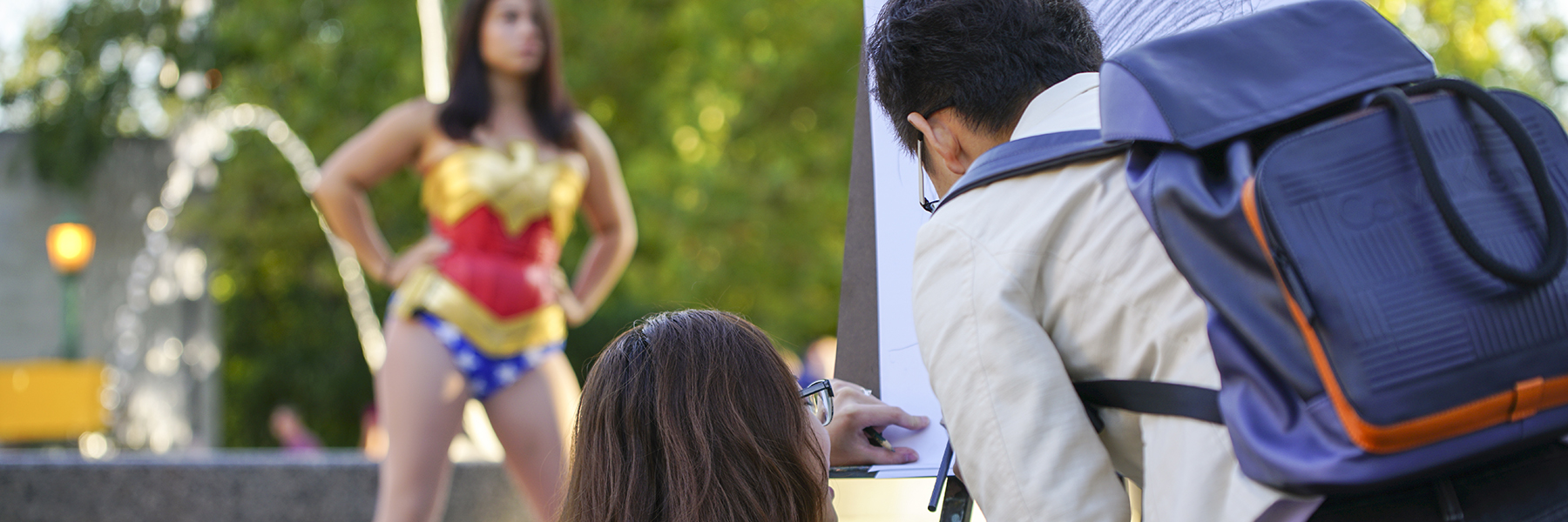 Two students draw a portrait of someone dressed as Wonder Woman.